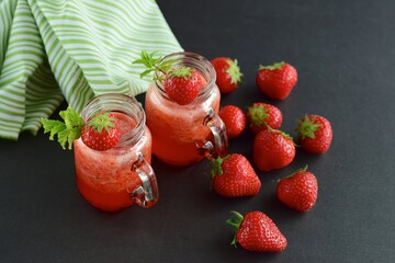 Fresh organic strawberry smoothie with mint in glass jar on black background