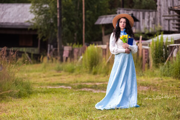 Fototapeta premium Beautiful Young caucasian Brunette Girl Posing in Old-fashioned Dress With Flowers. Reading Book Outdoor