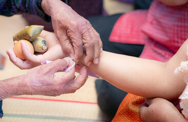 The ceremony of binding people’s wrist with the holy thread to console people's Kwan. Thai culture. Beliefs and local culture of Northeastern Thai people. Old person binding holy thread to Thai adult.