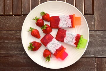 Homemade Vegan Strawberry Chia Coconut Milk Popsicles on wooden table. Summer dessert