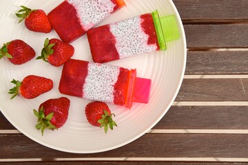 Homemade Vegan Strawberry Chia Coconut Milk Popsicles on wooden table. Summer dessert