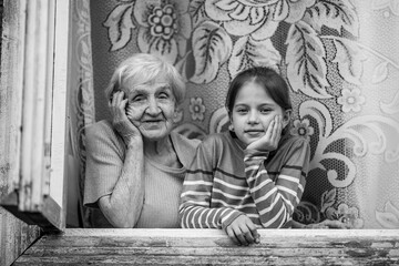 An old woman granny and her granddaughter together to look out the window. Black and white photo.