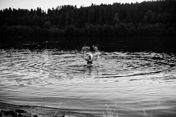 An old woman in the summer river at sunset. Black and white photo.