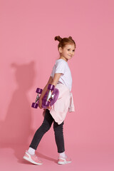 adorable little child girl with skateboard over pink background. Back view.