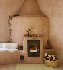 Charming inertia stove made of clay and pink plaster with lit fire and firewood basket