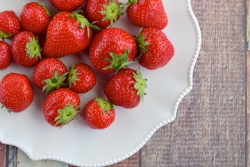 Fresh organic strawberry on white plate on wooden background. Flat lay