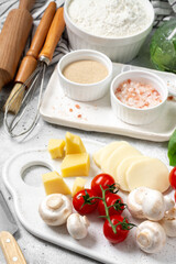 Pizza ingredients on a culinary background. Flour, yeast, salt, water, olive oil, parmesan, cheese, mozzarella, basil, tomatoes on the table. The concept of preparing for baking pizza or pie