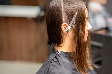 Fototapeta premium Close up side view of a young brunette caucasian woman with split hair in sections in a hair salon