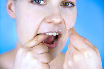 Woman brushing teeth with dental floss, close-up.