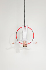 little child girl gymnast in white sportwear shows an acrobatic performance on an aerial hoop © Rychko Yevhen