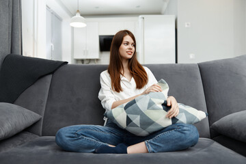 a cheerful woman is sitting in an apartment on a sofa with a pillow in her hands Comfort rest