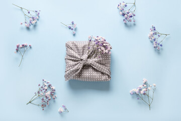 Spring eco-friendly gift wrapped in textile with fresh flowers on blue background. Sustainable gift. Traditional Japanese Furoshiki style. View from above.
