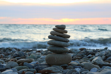 A group of rocks on the beach in nature. A pyramid of stones on a beach of pebbles, in the background a blurred background of the sea and sky at sunset, the concept of balance and harmony