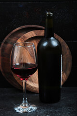 Bottle of wine with glass of wine on dark background with wooden plate