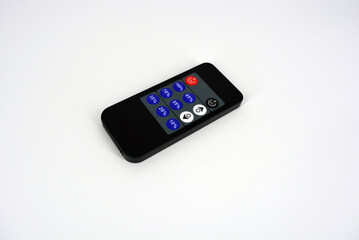 Black plastic radio remote control on batteries with colored buttons located on a white plastic background.