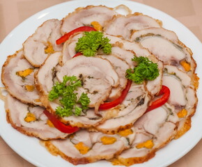 Sliced chicken roll with nut decorated with a sprig of parsley on a white ceramic plate close-up on a tablecloth background