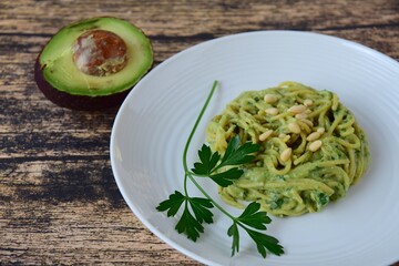 Gluten free chickpea spaghetti with avocado spinach pesto sauce garnish with parsley and pine nuts