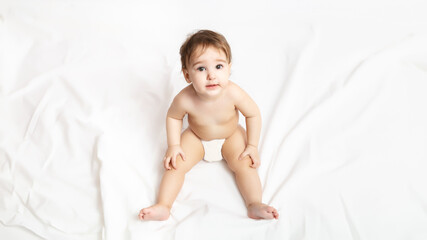 Funny little baby in a diaper. Portrait of a cute baby 9 months old sitting on a white blanket.