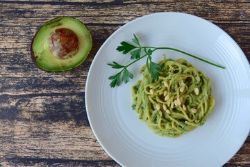 Gluten free chickpea spaghetti with avocado spinach pesto sauce garnish with parsley and pine nuts