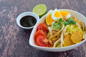 Soto Ayam, Indonesian food, yellow spicy chicken soup with vermicelli, fried potato, hard boiled egg and fried shallot.