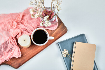 Notebooks and cup of coffee on the wooden board with flowers