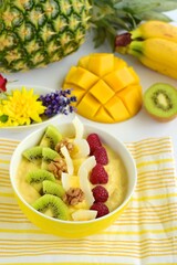 Mango banana pineapple smoothie bowl topped with raspberry, kiwi, walnut and coconut chips