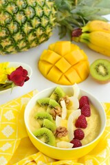 Mango banana pineapple smoothie bowl topped with raspberry, kiwi, walnut and coconut chips
