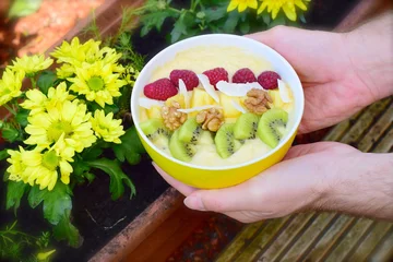Rollo Mango banana pineapple smoothie bowl topped with raspberry, kiwi, walnut and coconut chips © AmalliaEka