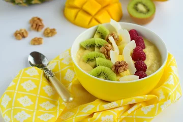 Fototapeten Mango banana pineapple smoothie bowl topped with raspberry, kiwi, walnut and coconut chips © AmalliaEka