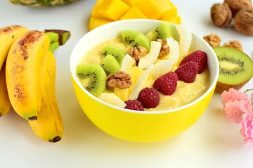 Selbstklebende Fototapeten Mango banana pineapple smoothie bowl topped with raspberry, kiwi, walnut and coconut chips © AmalliaEka