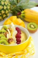 Mango banana pineapple smoothie bowl topped with raspberry, kiwi, walnut and coconut chips