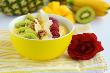 Mango banana pineapple smoothie bowl topped with raspberry, kiwi, walnut and coconut chips