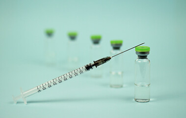 the syringe is lying on the ampoule with the vaccine. the syringe is in focus, the ampoules in the...
