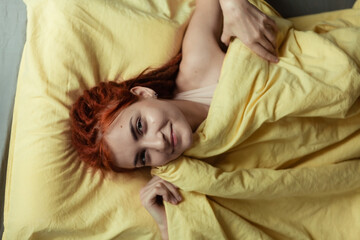 Obraz premium Very pretty redhead girl with dreads on bed in bedroom in the morning. A feminine, gentle girl. Healthcare and Sleep Concept.