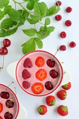Breakfast berry smoothie bowl topped with raspberry, strawberry and cherry on white background
