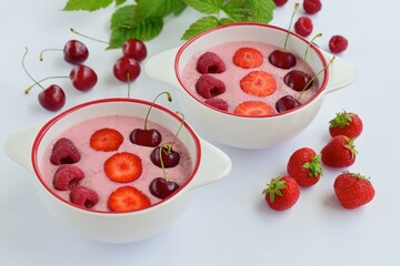 Breakfast berry smoothie bowl topped with raspberry, strawberry and cherry on white background