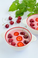 Breakfast berry smoothie bowl topped with raspberry, strawberry and cherry on white background