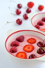 Breakfast berry smoothie bowl topped with raspberry, strawberry and cherry on white background