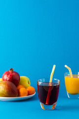 Delicious sweet citrus, mango and pomegranate juices in glasses and ripe fruits on a blue background