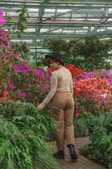 Obraz premium A beautiful plus size girl in a hat walking among the green plants of the greenhouse. Cottagecore style