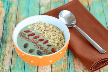 Nutritious green smoothie bowl with goji berries, oats, pumpkin seeds, sunflower seeds and flax seeds on green wood background. 
