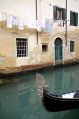 Fototapeta na wymiar Venice typical view of a canal with the bow of a passing gondola and the clothes hanging out to dry at a window