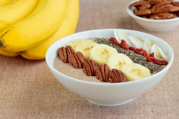 Chocolate smoothie bowl topped with banana, goji berry, pecan nuts, coconut chips and chia seeds