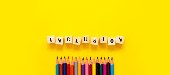 Inclusion banner word on wooden cubes and pencils on yellow background