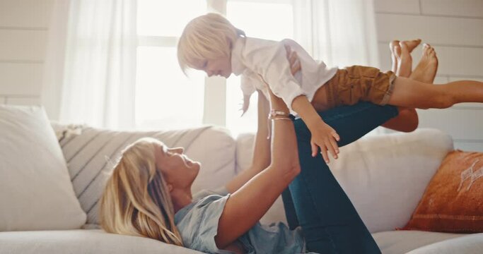 Mother and cute son spend quality time together at home, playing on the couch, pretending to fly, laughing and smiling, quality family time