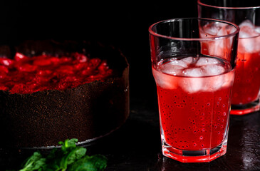 Amazing composition with strawberry cheesecake and strawberry drink with rosemary. Only part of the cheesecake in focus and a particle of a glass of drink.