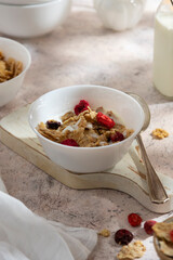 Corn flakes with strawberry and blueberry in black bowls over dark background, top view.