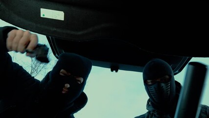 View from inside the trunk of the car. Two kidnappers threaten with a gun and a baseball bat - Powered by Adobe