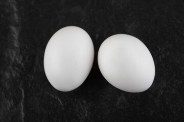 Two fresh white chicken eggs on a black background