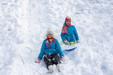 Two girls rolled down the hill and sitting in the snow joyfully look into the frame